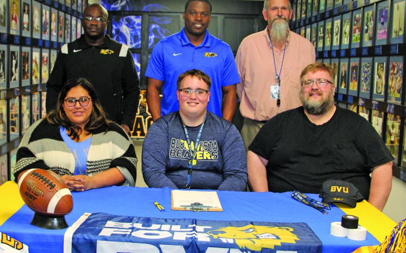 Sentinel photo/Mike Reddell Bay City Blackcat offensive lineman Isaac Allen officially signed with Buena Vista University, Storm Lake, Iowa, in a ceremony last week. Allen, center, is flanked by his parents, Yvette Allen, at left, and his father, Jonathan Allen. His mother is the late Michelle N. Allen. Also a powerlifter, Isaac aspires to become a coach. His coaches, second row from left: are Offensive Coordinator Anthony Smith, Head Coach Robert Jones, Head Powerlifting Coach Ron Arnesen.