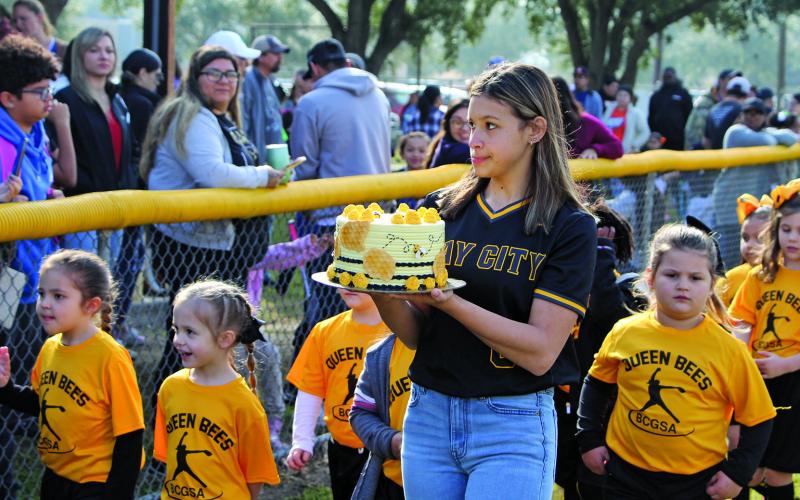Sentinel photo/Mike Reddell The Queen Bees were on parade Saturday morning, Feb. 12, for Bay City Girls Softball Association’s opening days ceremonies. A Ladycat softball player holds a Queen Bee cake for the teams’ auction fundraiser, with County Judge Nate McDonald serving as auctioneer.