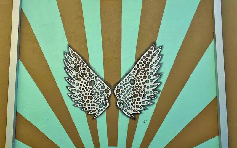 Photo/Zeinab Ghais Check out Ghais’ wings on the East alleyway of The Burlap Sack Boutique and CoastalGlo. Ghais wanted to design a mural that incorporated both businesses. There is a sun motif behind a pair of “Lace” wings.