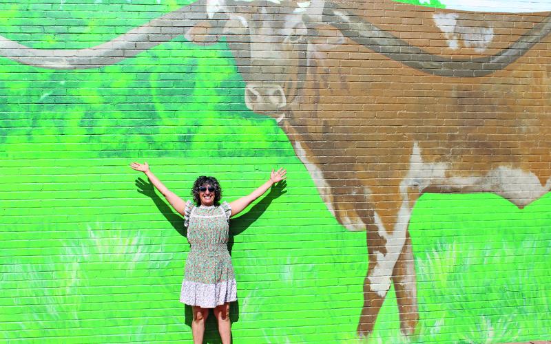 Sentinel Photo/Jessica Shepard Bay City artist Zeinab Ghais poses beneath her work-in-progress mural featuring Guinness Book of Records “Longest Longhorn Steer” 2018 winner “Sato" last Friday. Ghais has been working on the mural for almost a month and is using "point of perspective painting" to achieve a realistic look to her portrayal of the steer.