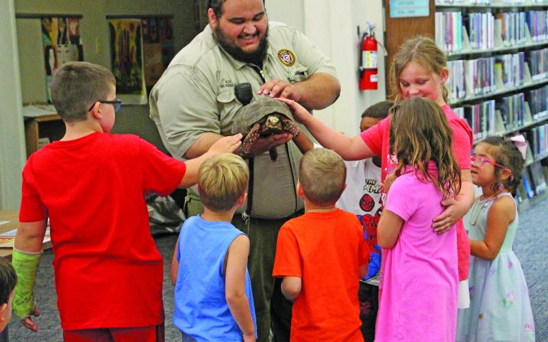 Sentinel photo/Jessica Shepard Bay City Animal Control Officer Miguel Mirelez showed off Annie the Red-footed Tortoise, center, to a group of youngsters at Bay City Public Library's "Tails and Tales" event last week. Mirelez gave tips on keeping pets and wildlife safe during the summer and cautioned children to get an adult if there is something wrong with an animal so that Animal Control can be notified.