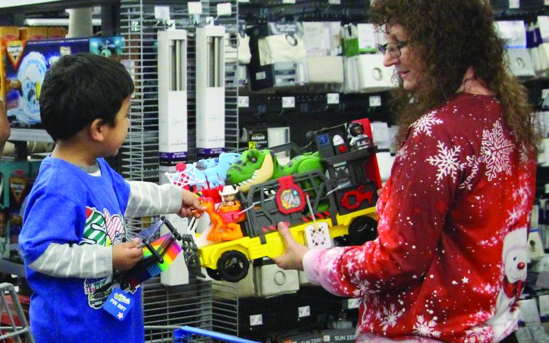 Sentinel Photo/Jessica Shepard Crystal Folse helps a youngster with a toy selection at the Dec. 11 Shop with a Cop at Walmart. Approximately 40 kids got to pick out a batch of Christmas presents.