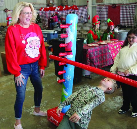 Gena Lea Smith, Van Vleck High School’s Theater Director, laughs watching a boy’s successful maneuver under the limbo bar at Bay City's annual Santa's Fly-In event Dec. 11, at Bay City Regional Airport. It was a free, festive morning with storytime, milk & cookies. Bay City Public Library, Bay City Regional Airport, and Van Vleck Leopard Players partnered in the event. Sentinel Photo/Mike Reddell