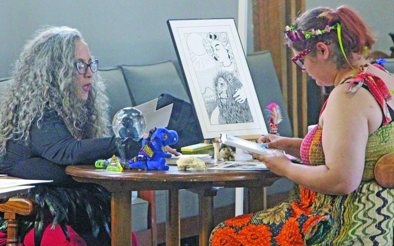 Local artist Lizbeth Davis, left, explains her art to a prospective customer during the Art League of Bay City's “Mystic Realms ArtWalk 2026” on Aug. 15. Sentinel Photo/ Jessica Shepard