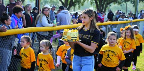 Sentinel photo/Mike Reddell The Queen Bees were on parade Saturday morning, Feb. 12, for Bay City Girls Softball Association’s opening days ceremonies. A Ladycat softball player holds a Queen Bee cake for the teams’ auction fundraiser, with County Judge Nate McDonald serving as auctioneer.