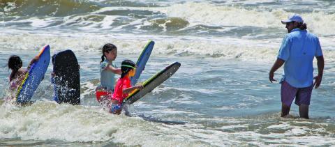 Sentinel photo/Mike Reddell A father awaits his flock of boogie boarders to teach them what waves to catch at Matagorda Beach during the Fourth of July weekend.