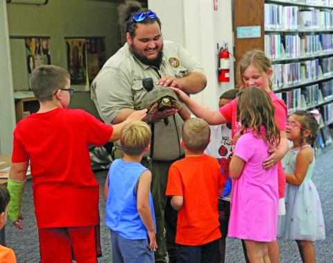 Sentinel photo/Jessica Shepard Bay City Animal Control Officer Miguel Mirelez showed off Annie the Red-footed Tortoise, center, to a group of youngsters at Bay City Public Library's "Tails and Tales" event last week. Mirelez gave tips on keeping pets and wildlife safe during the summer and cautioned children to get an adult if there is something wrong with an animal so that Animal Control can be notified.