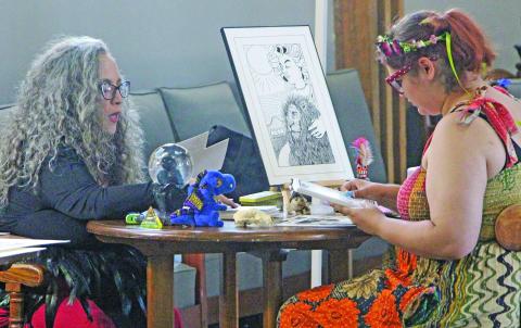 Local artist Lizbeth Davis, left, explains her art to a prospective customer during the Art League of Bay City's “Mystic Realms ArtWalk 2026” on Aug. 15. Sentinel Photo/ Jessica Shepard