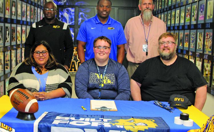 Sentinel photo/Mike Reddell Bay City Blackcat offensive lineman Isaac Allen officially signed with Buena Vista University, Storm Lake, Iowa, in a ceremony last week. Allen, center, is flanked by his parents, Yvette Allen, at left, and his father, Jonathan Allen. His mother is the late Michelle N. Allen. Also a powerlifter, Isaac aspires to become a coach. His coaches, second row from left: are Offensive Coordinator Anthony Smith, Head Coach Robert Jones, Head Powerlifting Coach Ron Arnesen.