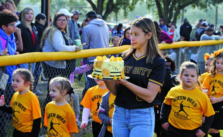 Sentinel photo/Mike Reddell The Queen Bees were on parade Saturday morning, Feb. 12, for Bay City Girls Softball Association’s opening days ceremonies. A Ladycat softball player holds a Queen Bee cake for the teams’ auction fundraiser, with County Judge Nate McDonald serving as auctioneer.